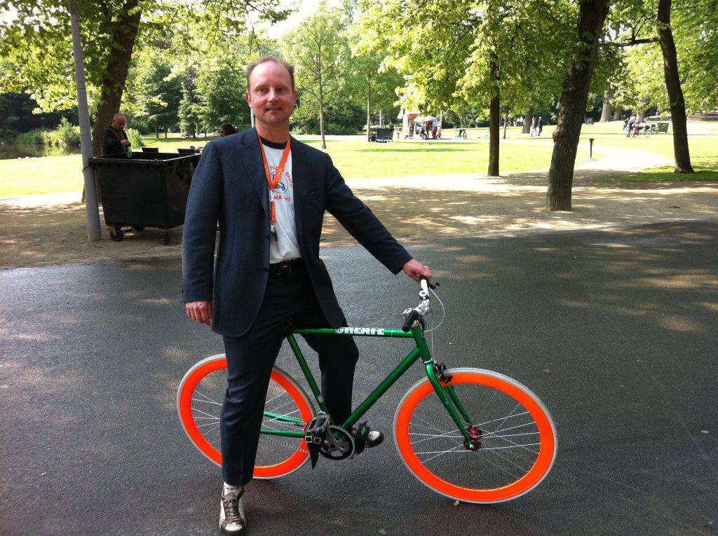 Lex van Buuren zegt op een fiets met oranje velgen dat hij graag reisleider en lokale gids wil zijn tijdens het EK Voetbal 2020 in Amsterdam. Bijvoorbeeld voor Franstalige groepen.
