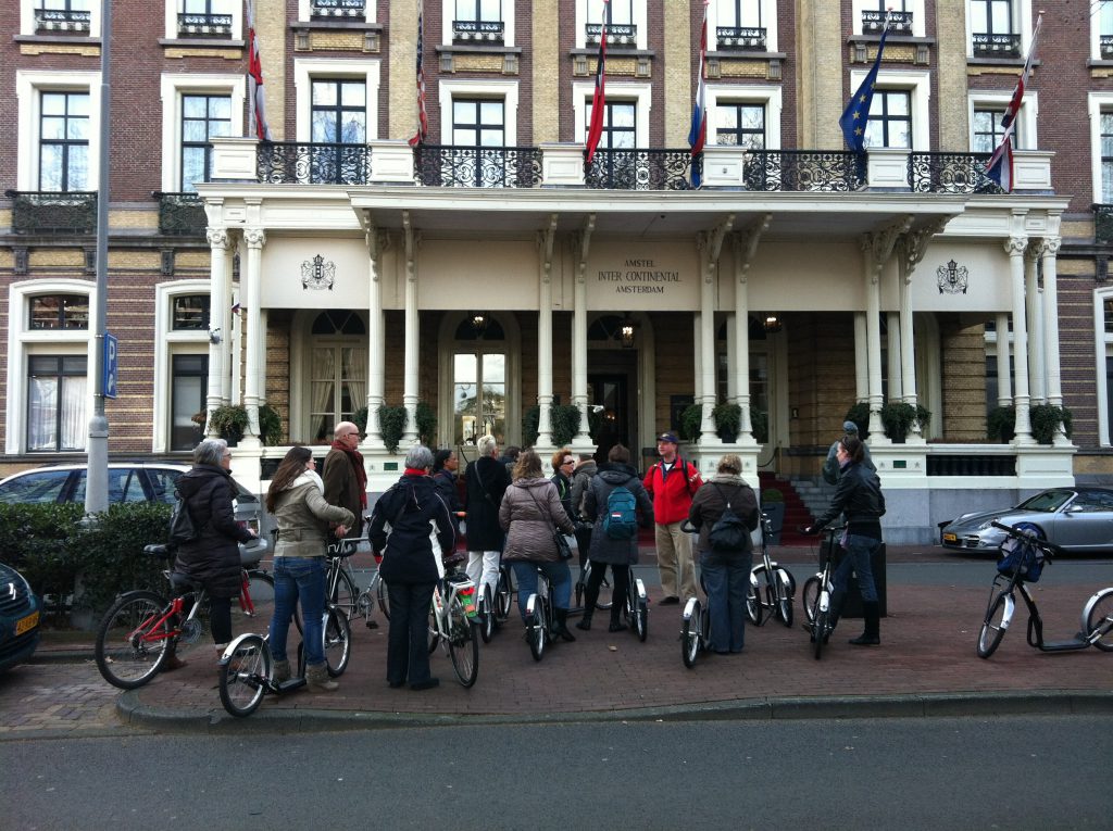 Eén van de stepgidsen van Lex and the City stopt met de groep voor het Amstel Hotel voor een anekdote tijdens deze ongebruikelijke Amsterdamse stadsrondleiding